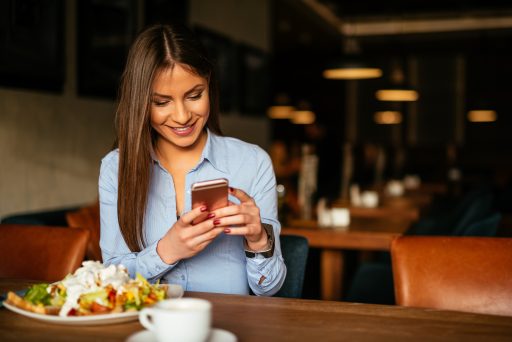 Beautiful woman having breakfast and texting on a mobile phone.